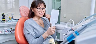 Happy dental patient using mirror to admire her new bridge