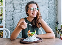 Woman eating yogurt with fruit at a table smiling