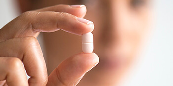 Woman holding pill in foreground to illustrate antibiotic therapy