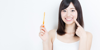 Woman with toothbrush pointing to bright white smile